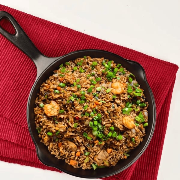 Shrimp fried rice with chopped green onions and vegetables in a black pan on a red placemat.