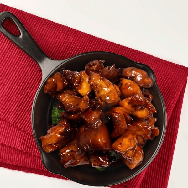 Sweet and sour chicken in a black skillet on a red placemat.