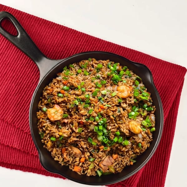 Shrimp fried rice with chopped green onions, carrots, and other vegetables in a black pan.