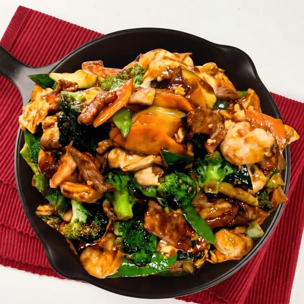 Stir-fried chicken, beef, and shrimp with broccoli, carrots, and snow peas in a black pan.