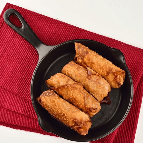 Four crispy golden egg rolls in a black skillet on a red placemat.