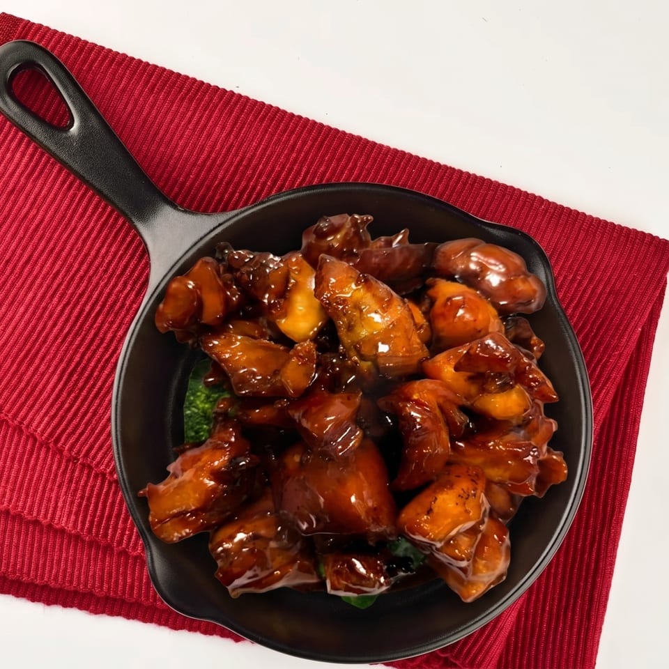 Sweet and sour chicken with broccoli in a black skillet on a red placemat.
