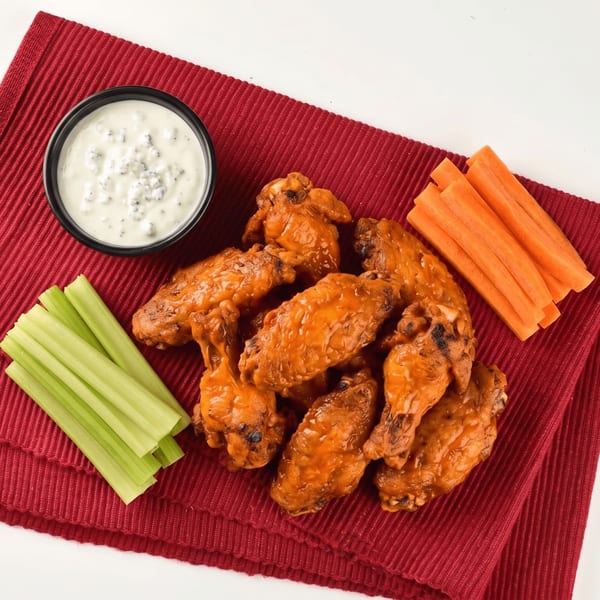 Buffalo wings with blue cheese dip, celery sticks, and carrot sticks on a red placemat.